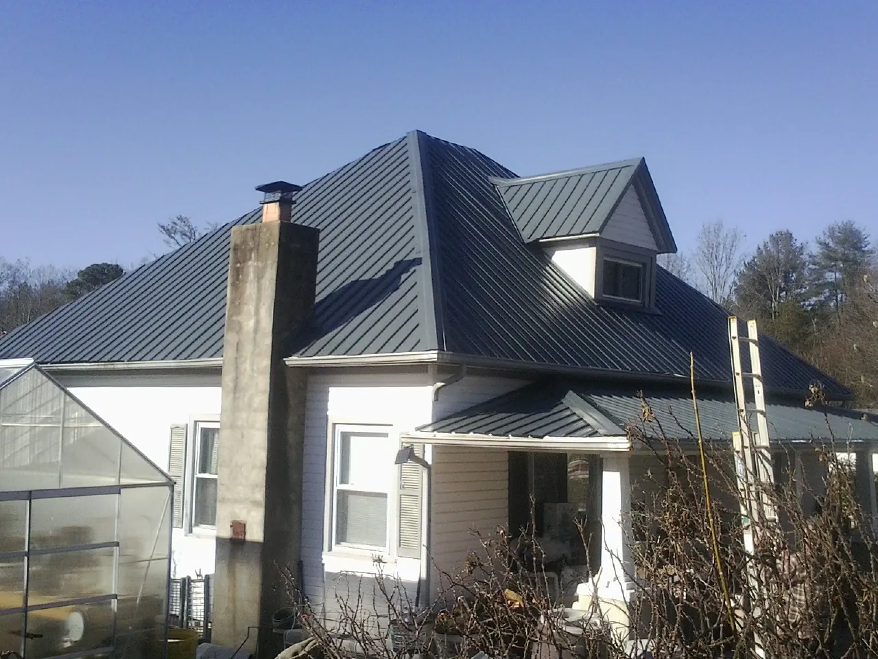 Dark blue standing seam metal roof on a white farmhouse with dormer — Slate & Tile Roof Repair by Roofing Brothers in Donahue
