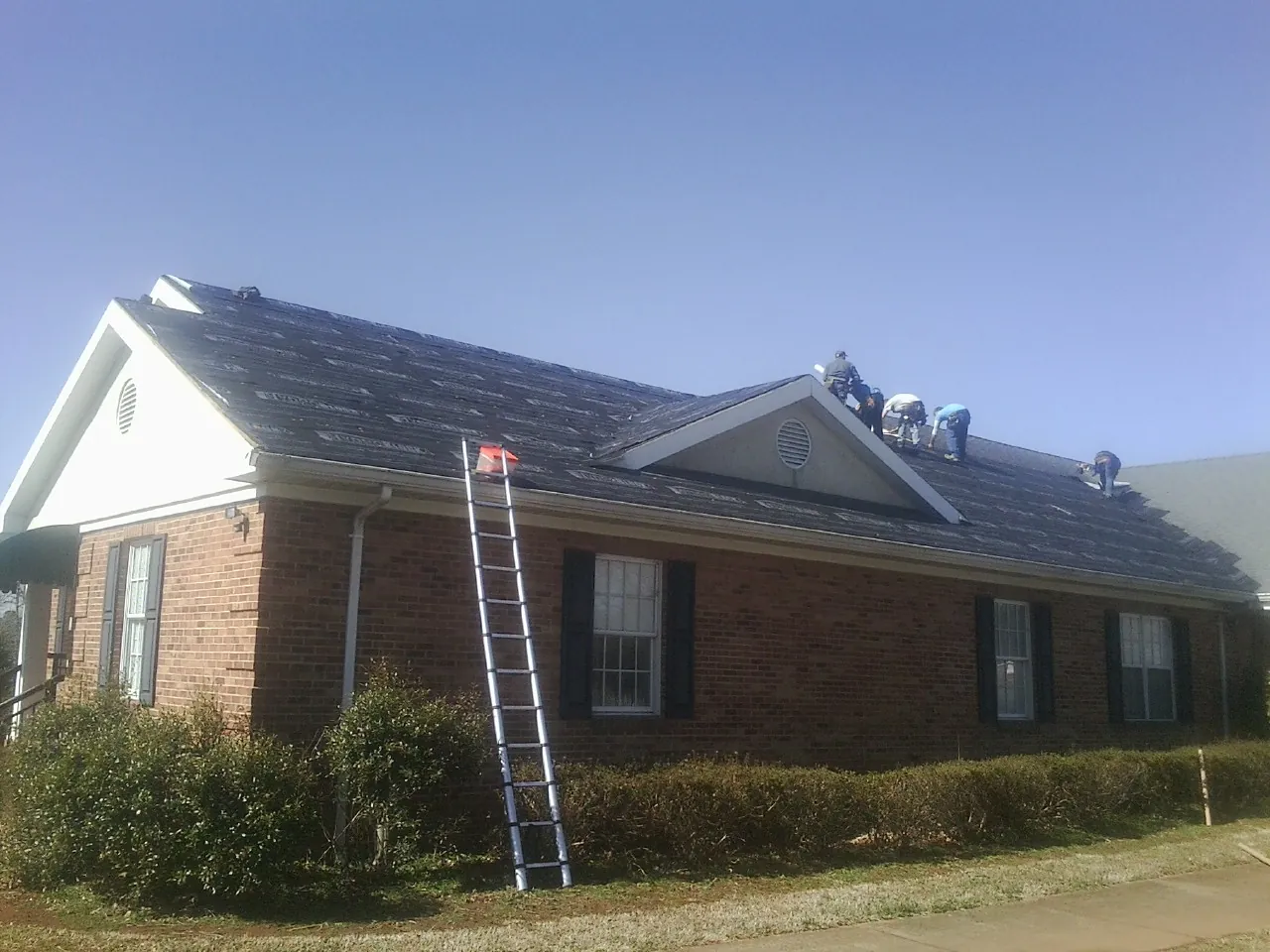Crew tearing shingles off a brick ranch roof with a ladder set — Emergency Roof Repair work by our crew in Donahue
