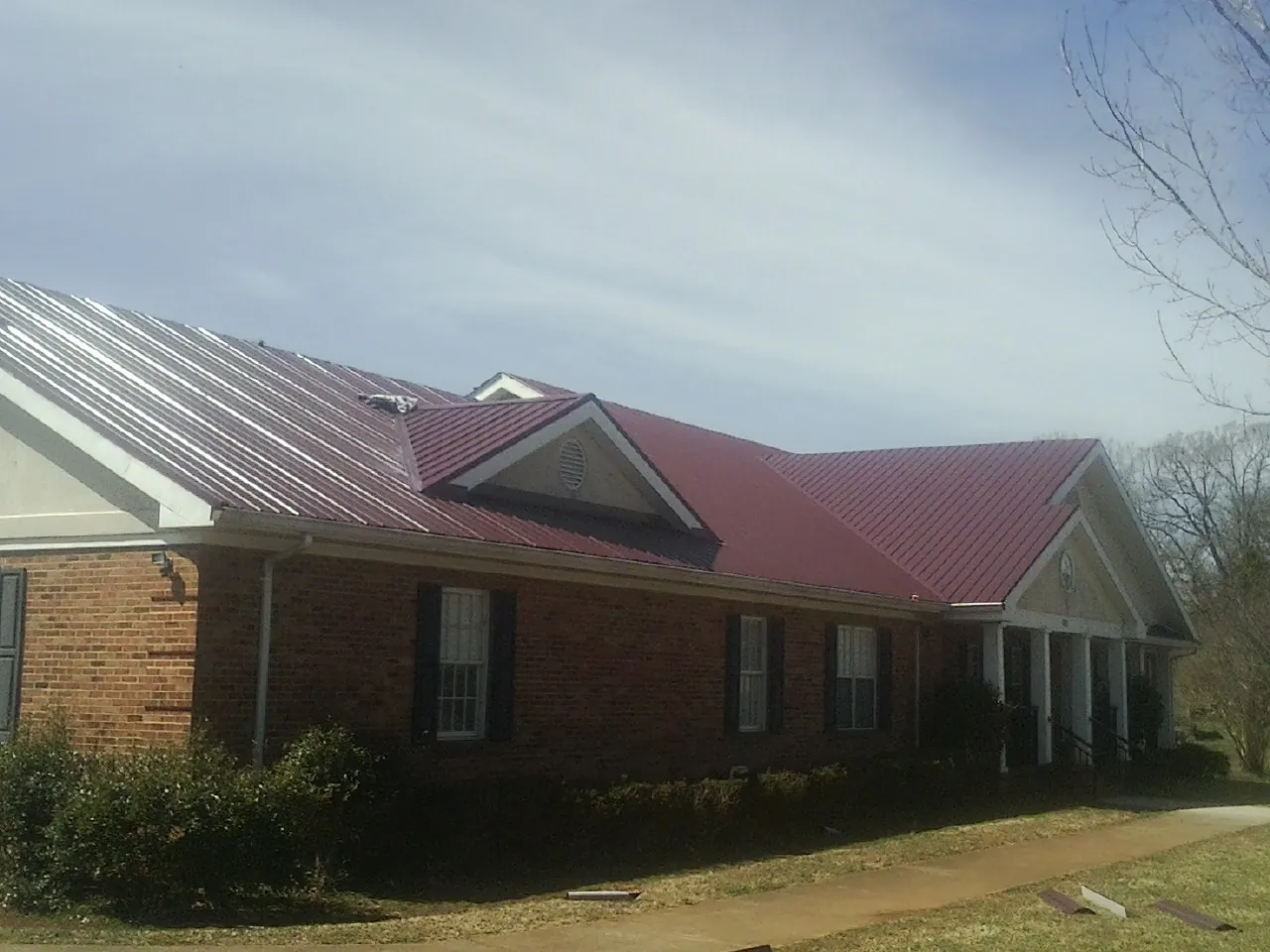 Red metal roof with gabled entries on a long brick building, from a Hail Damage Roof Repair job in Donahue
