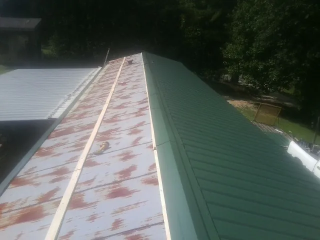 Old rusted panels beside newly installed green metal roofing — Wind Damage Roof Repair by Roofing Brothers in Donahue