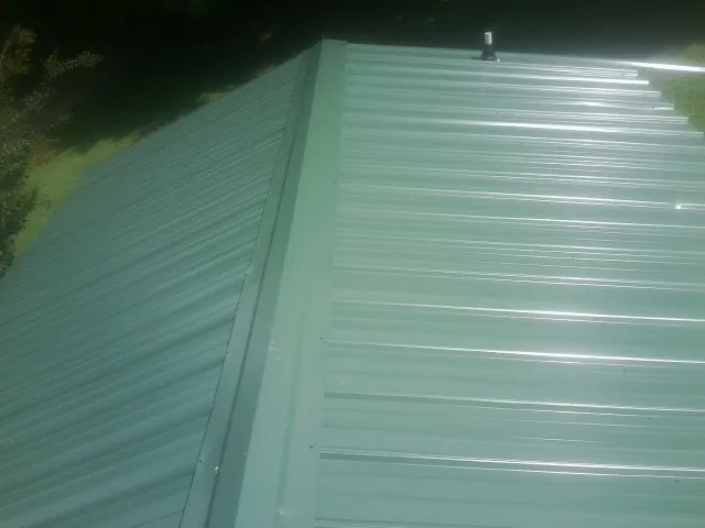 New green metal panels meeting at the ridge of a roof — Flat Roof Repair work by our crew in Donahue