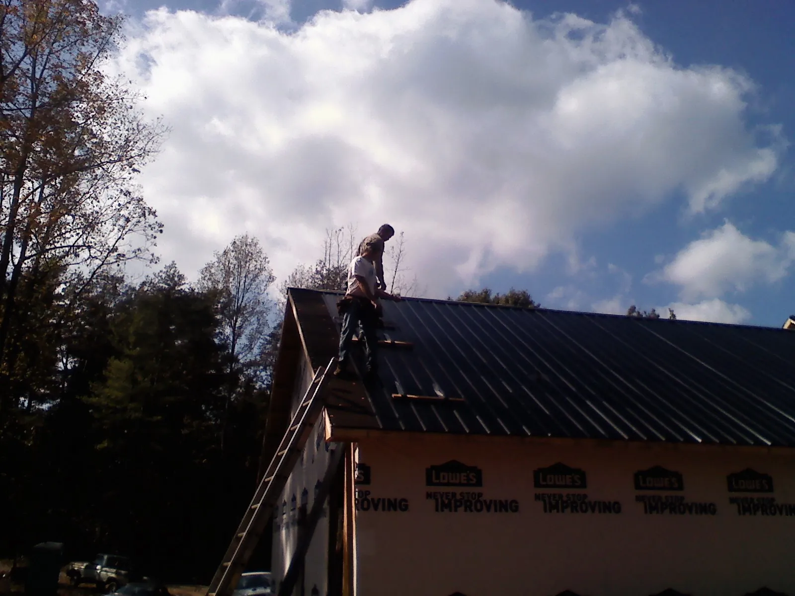 Roofer fastening dark metal panels high against a cloudy sky, from a Roof Inspection job in Donahue