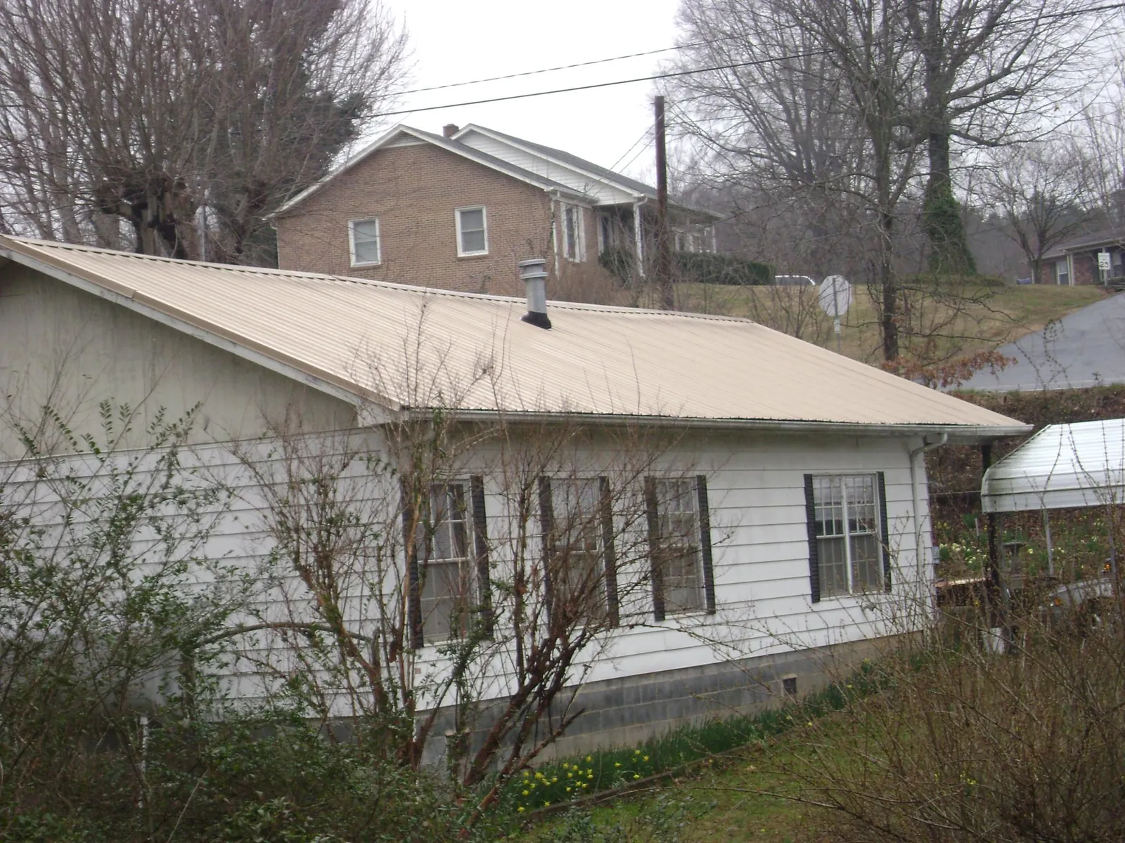 Tan metal roof on a white sided house set into a hillside — Commercial Roofing by Roofing Brothers in Donahue