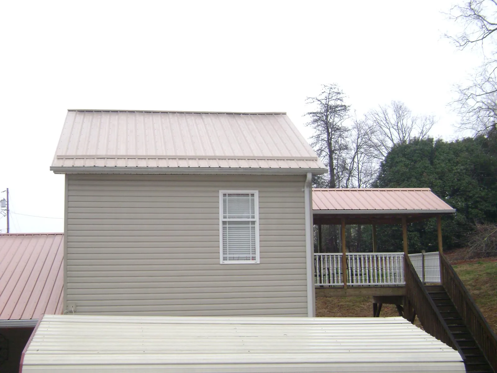 Tan metal roofs on a two story addition and attached porch, from a Roof Replacement job in Donahue