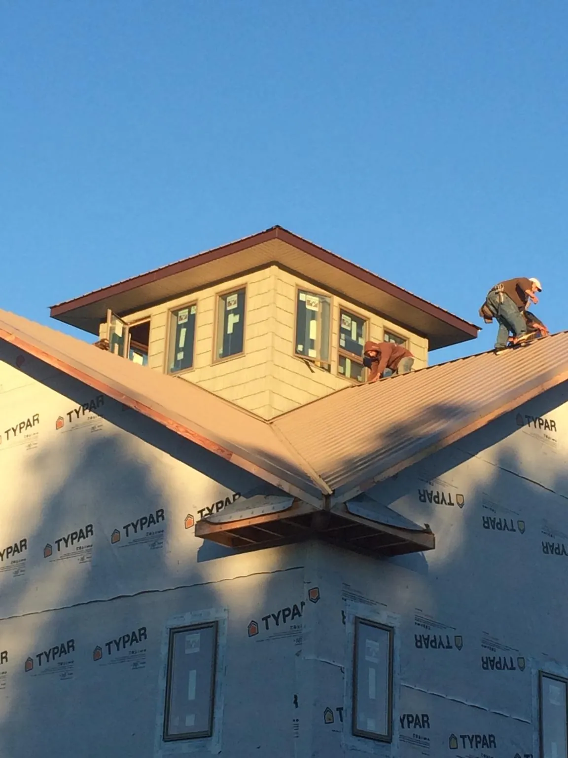 Roofers working around a rooftop cupola on a new metal roof at sunset — Roof Waterproofing in Donahue by Roofing Brothers